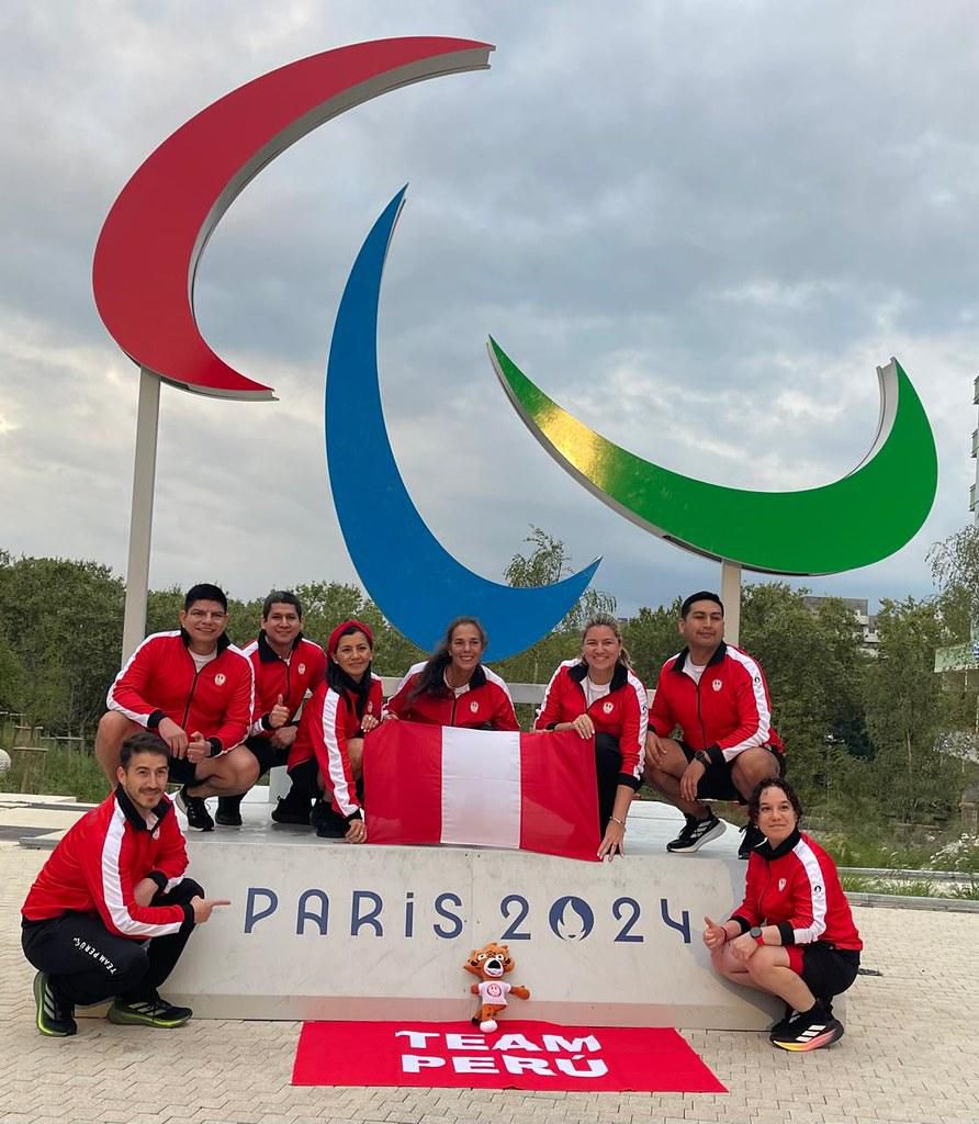 Integrantes del Team Perú posan con la bandera frente al símbolo paralímpico